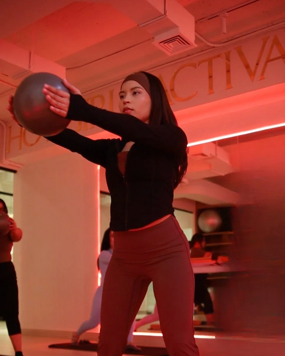 Una alumna en la sala templada sosteniendo un balón, con la luz roja de fondo.
